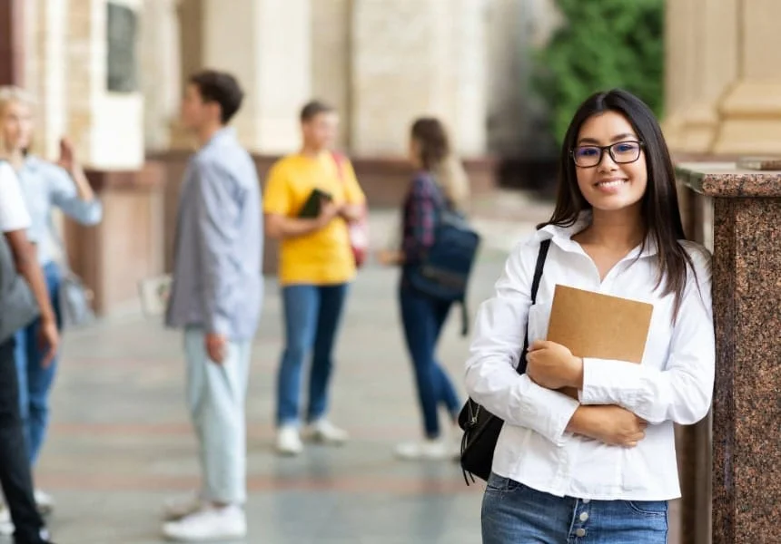 university student holding books whilst other students talk in the background