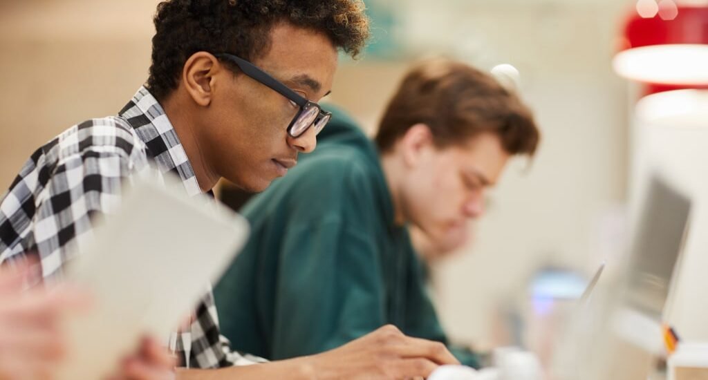 2 Computer science students in a university class, sitting at their desks and typing on their computers.