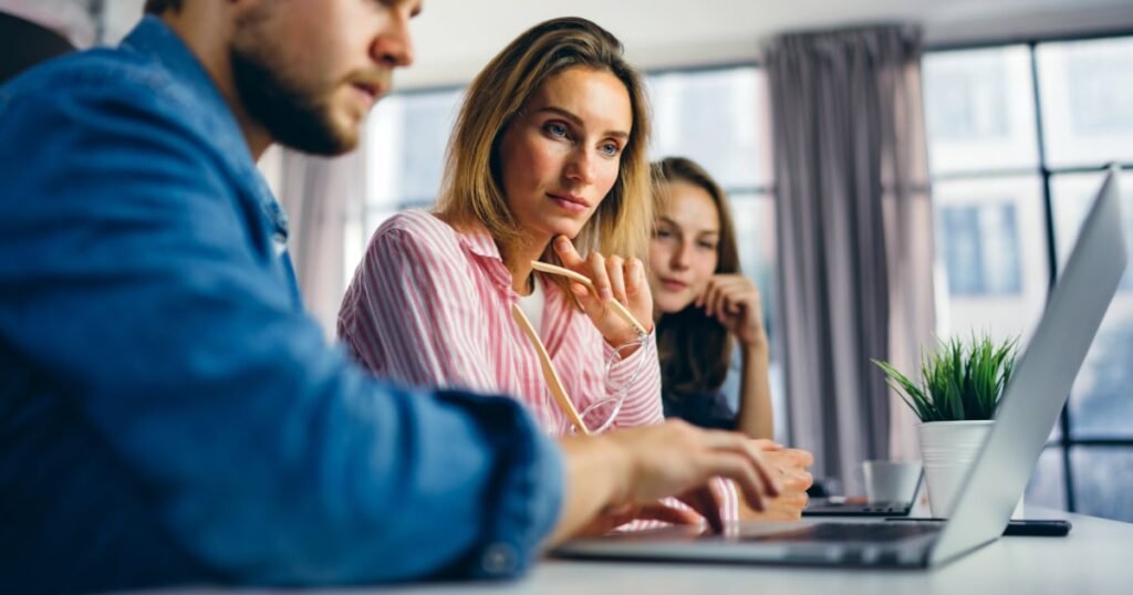 1 male and 2 female students working at a business studies project with a laptop while sitting at a desk.